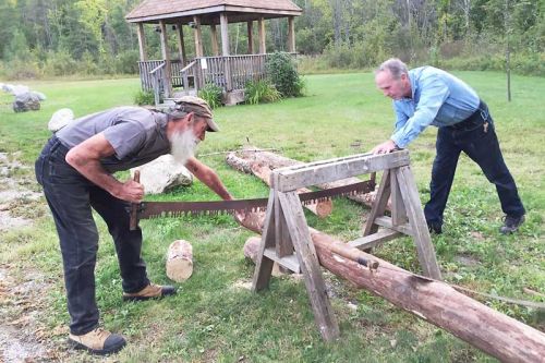 Wayne Murkar and Leonard Emery trying out the two-person saw at the history discussion, “Free Land in Ompah”, on Friday night.