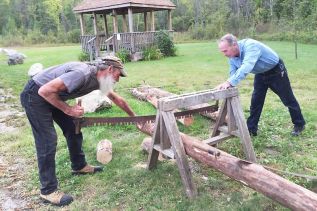 Wayne Murkar and Leonard Emery trying out the two-person saw at the history discussion, “Free Land in Ompah”, on Friday night.