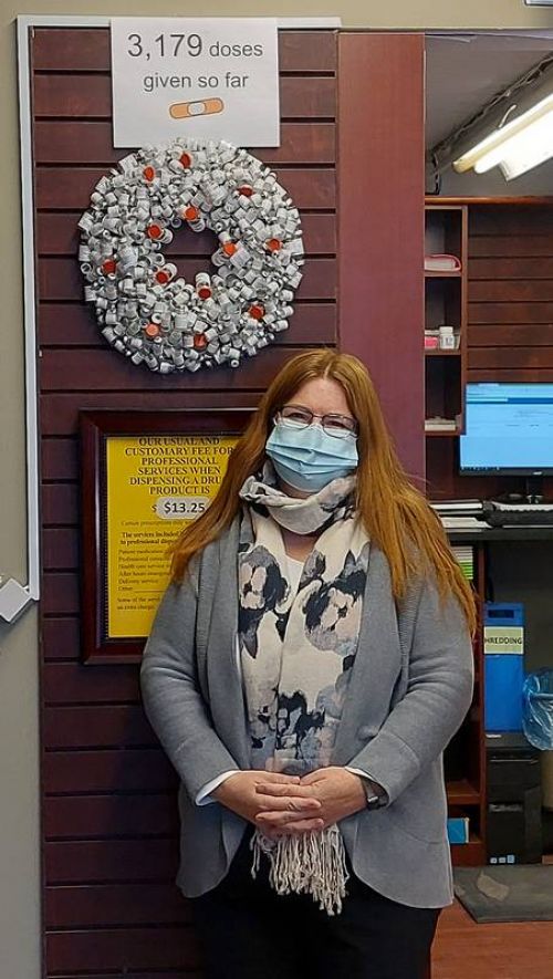 Sarah Swanson, in front of the ever growing vaccine vial wreath that was created by Sharbot Lake Pharmacy staff.