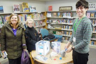 KFPL Sharbot Lake patrons Lin Hannah and Emily Baillargeon learn about 3D printing from KFPL tech tutor Derek Fenlon