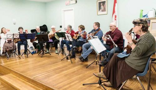 Tunes 'n Tea, a ukulele band led by Sandi Brown.  Enthusiastic members are (left to right) Kim Brown and Baby Stella, Kathleen Cox, Roxanne Bradshaw, Carolyn McCulloch, Gloria Gonin, Sandi Brown, Keith Brown, Dennis Perry, Cathy Hook and Lynne Young; photo by Ken Hook. 